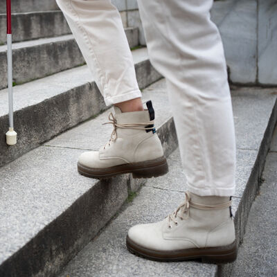 Bild vergr&ouml;&szlig;ern: Eine Person läuft eine Treppe hinauf. Die nächste Stufe wird mit einem Langstock berührt.