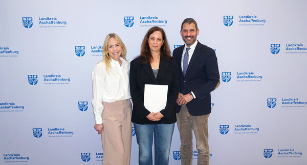 Bild vergr&ouml;&szlig;ern: Die drei Personen posieren neben einander stehend für das Foto, während die Person in der Mitte eine Urkunde hält