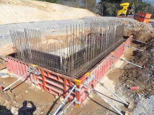 In einer Baugrube befindet sich eine kniehohe Schalung, die von Metallstreben gestützt wirde. Aus dem umschalten Bereich ragen Metallstreben hervor.