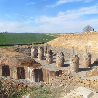 Bild vergr&ouml;&szlig;ern: Der Weitblick über die Baustelle zeigt sechs massive Säulen, die aus dem Boden ragen, wobei aus deren Spitzen wiederum Metallstreben ragen.