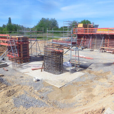 Bild vergr&ouml;&szlig;ern: Auf einer teils erdenen und teils geschotterten Fläche sieht man zum einen Säulen, die bislang nur aus Betonstahlstreben bestehen, und zum anderen Teile, die bereits auch schon verschalt wurden, um denn mit Beton gefüllt zu werden.