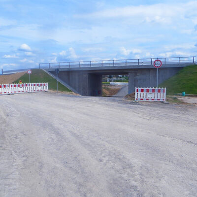 Bild vergr&ouml;&szlig;ern: Unter blauem Himmel sieht man eine fertig gestellte Brücke, unter der ein befahrbarer Weg hindurch führt.