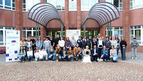 Bild vergr&ouml;&szlig;ern: Die zig Mitglieder des Jugend-Kreistags posieren stehen beziehungsweise hocken neben einander und posieren für das Foto vor dem Haupteingang des Landratsamts.