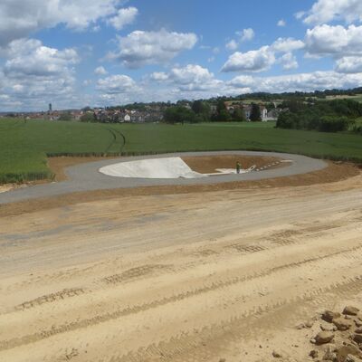 Bild vergr&ouml;&szlig;ern: Hinter einem erdigen Baufeld sieht man eine Vertiefung im Boden